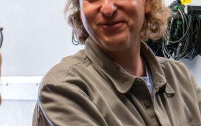 ein Mann und eine Frau sind im Vordergrund im Gespräch, ein Mann steht lachend im Hintergrund
