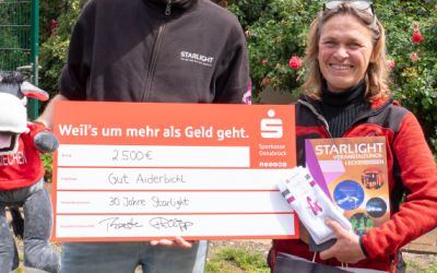 Ein Mann und eine Frau halten eine Spendentafel mit einem eingetragenen Betrag von 2.500 Euro hoch