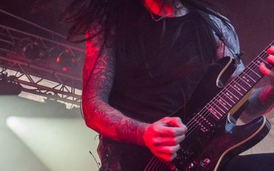 Ein Mann mit dunklen langen Haaren spielt auf einer beleuchteten Bühne Gitarre