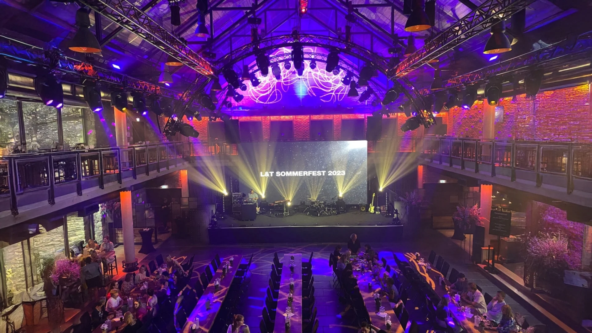 Sommerfest L+T im Jahr 2023 mit Blick von der Empore auf die Bühne und den Festsaal mit Tischreihen.