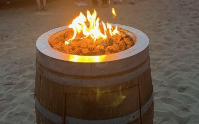 Eine angezündete Fassfeuertonne im Sand bei einer Beach-Party.