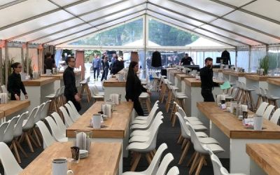 Partyzelt für Catering-Event mit holzfarbenen Tischen und weißen Stühlen.