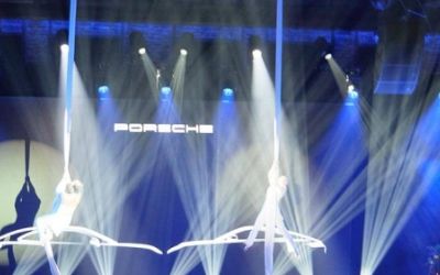 Event Porsche. Akrobaten schweben an Seilen über einer blau beleuchteten Bühne.