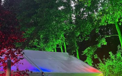 Bunt beleuchtetes Partyzelt und farbig angeleuchtete Bäume in einem Garten.